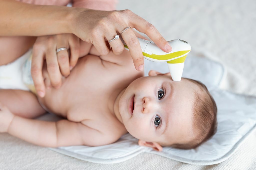 Baby on a play mat as gentle hands support them during an ear thermometer check—practical toddler care tip.