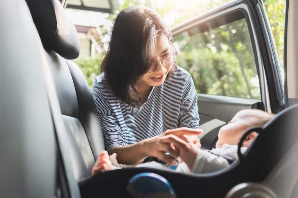 Mother securing her baby into a car seat in the back of the car