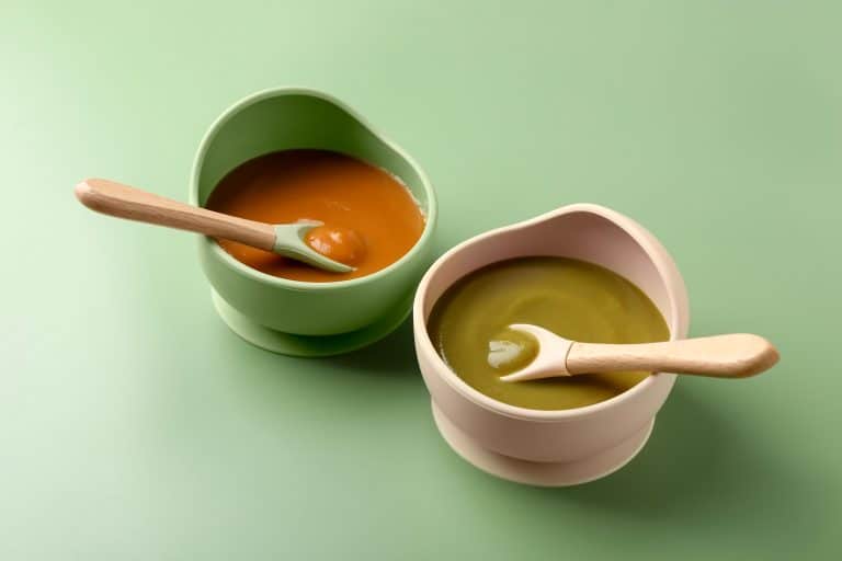Green and pink baby bowls with pureed food and wooden-handled spoons on a light green surface; baby feeding products Australia.