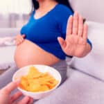 Pregnant woman holding up her hand to refuse a bowl of chips offered to her
