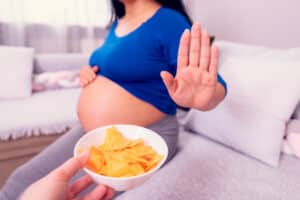 Pregnant woman holding up her hand to refuse a bowl of chips offered to her