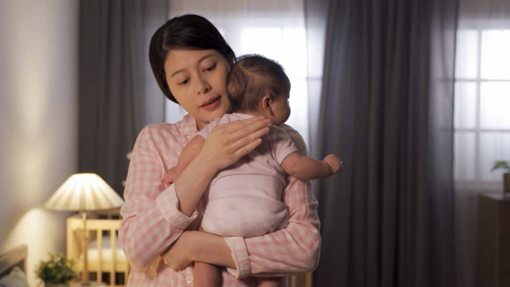 Mother gently patting and soothing her baby to sleep at night
