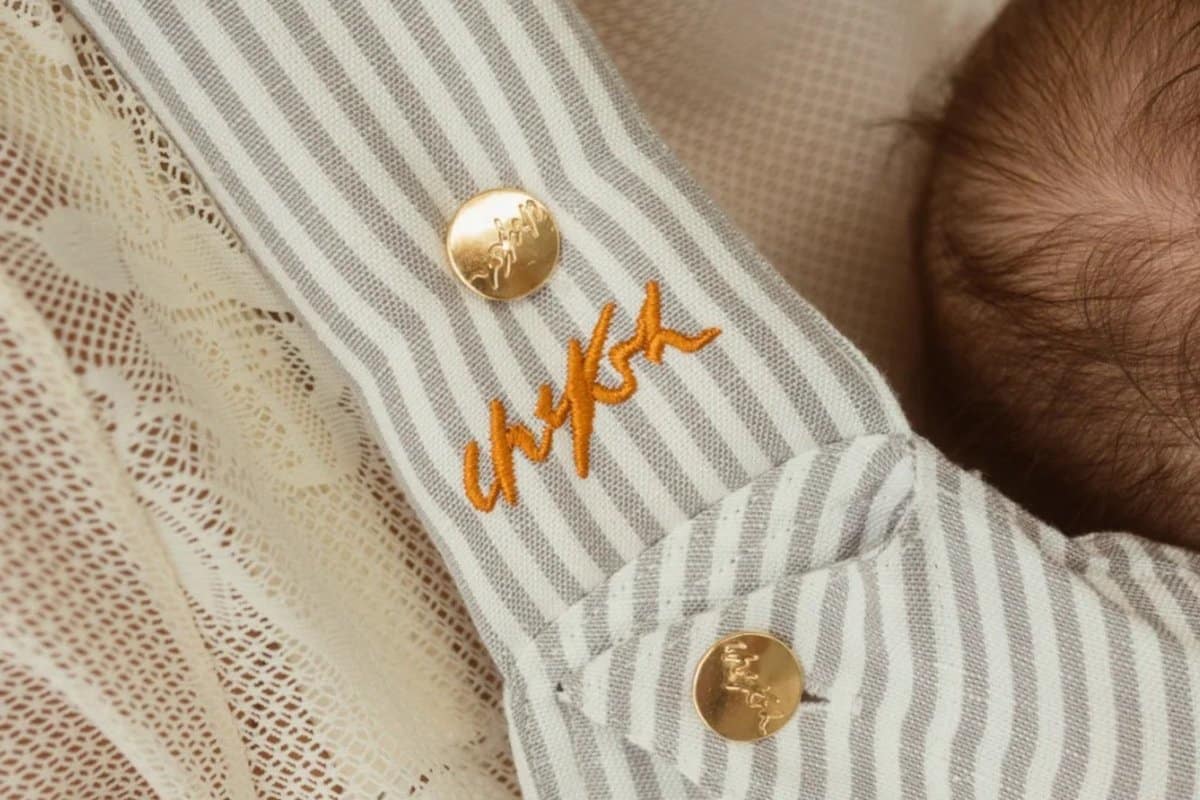 Close-up of the Chekoh Grey Stripe carrier strap with gold logo buttons and embroidered Chekoh logo
