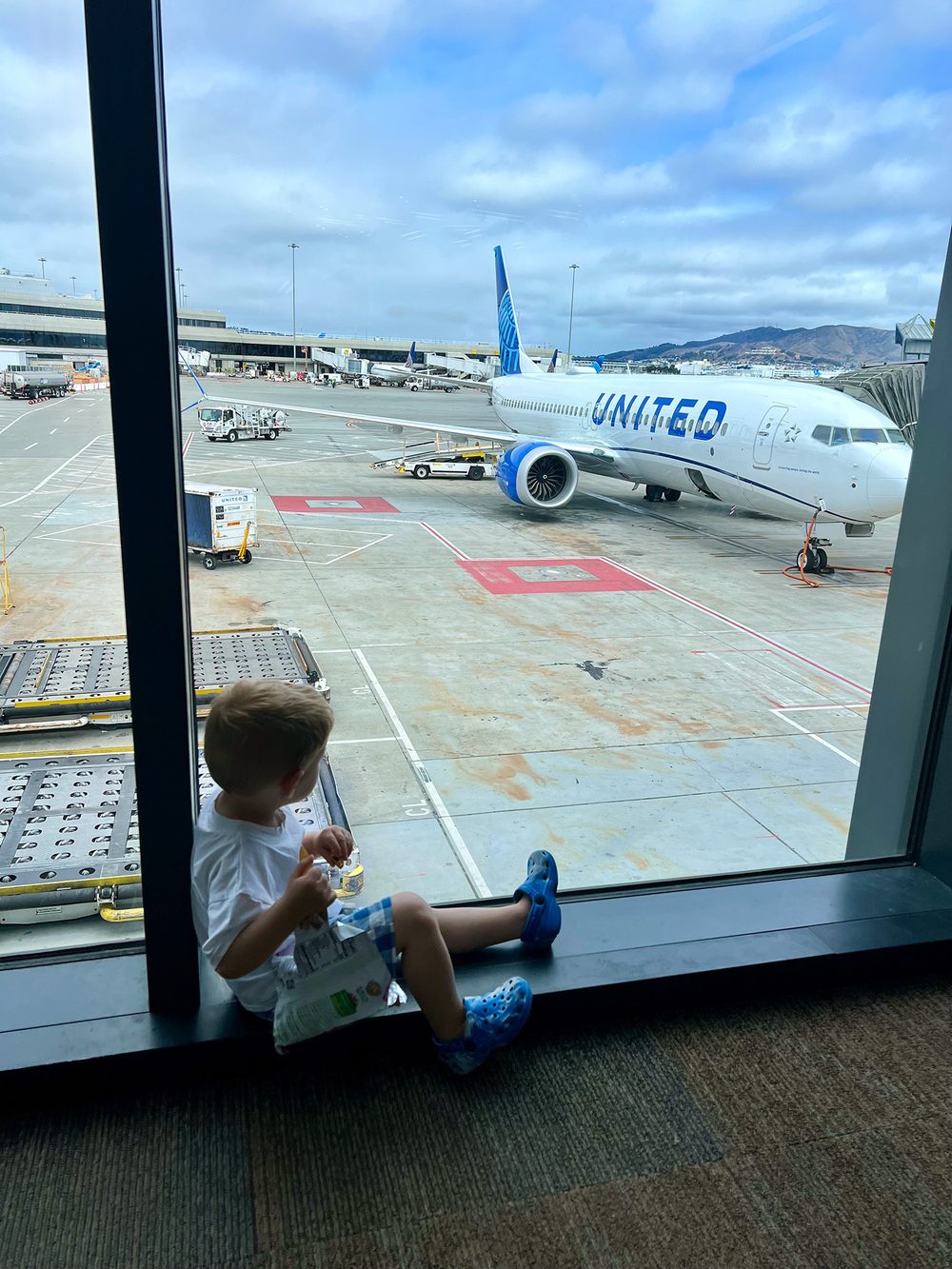 Toddler having a snack while watching a United plane from the airport window